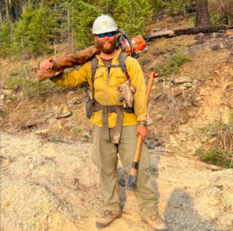 The speaker standing in a forest with wildland firefighting equipment