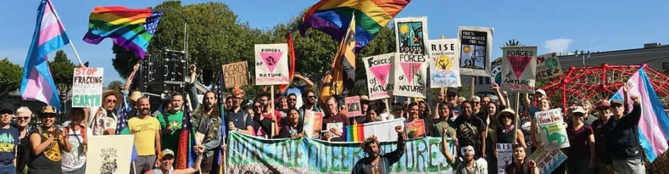 Climate justice protesters wave pride flags and signs