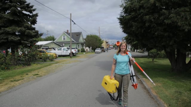 A Sustainable Communities Partnership student carries surveying equipment down a city street