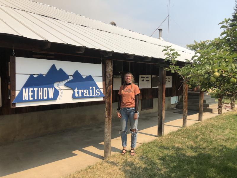 Student Zoe Hemez poses by the sign for her practicum organization, Methow Trails
