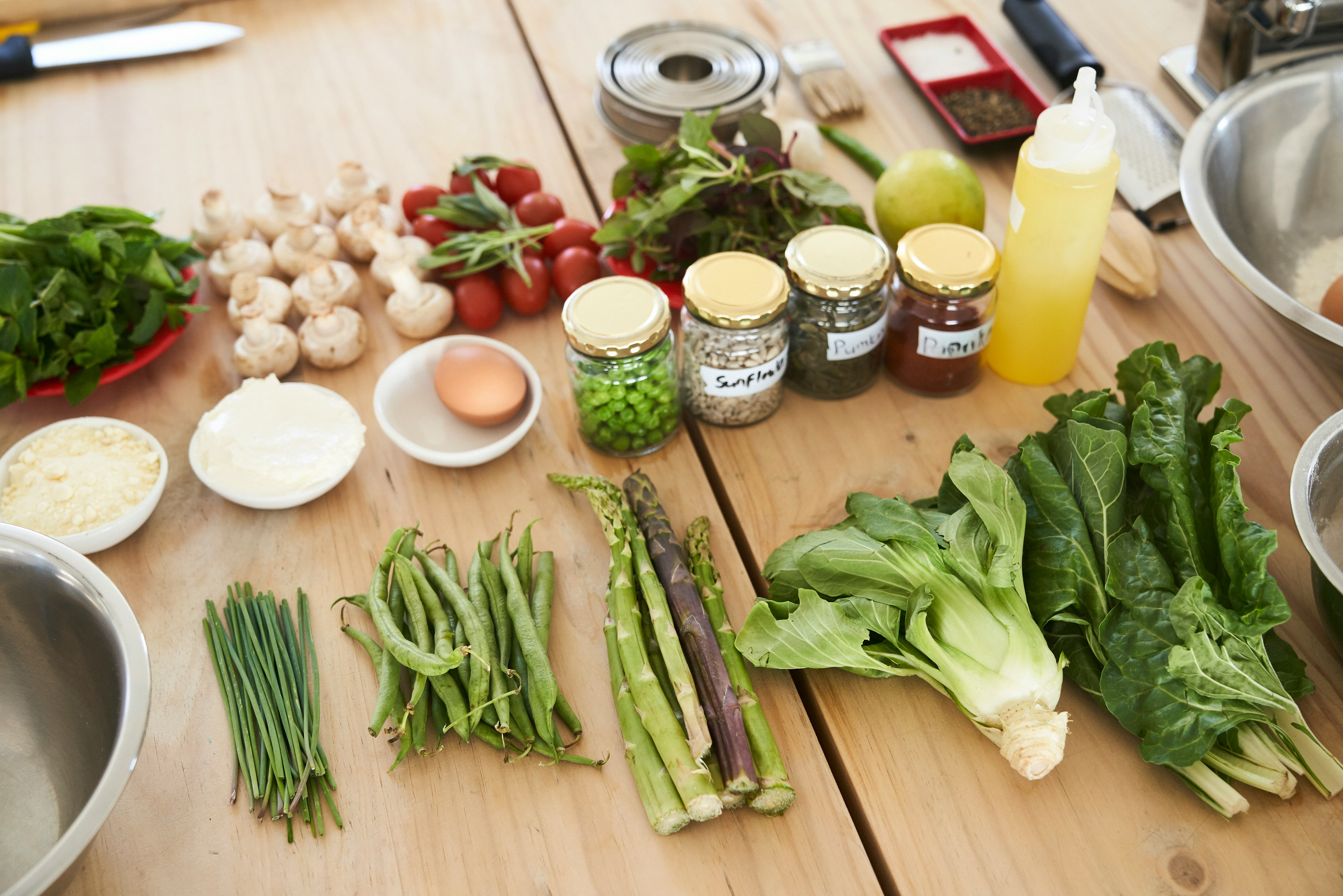 Green vegetables, an egg, tomatoes, and an oil laid out on a table for cooking.